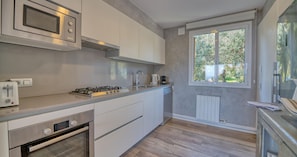 Eine moderne Küche mit eingebauter Mikrowelle, Gasherd und Backofen, einem Fenster mit Blick auf Grünflächen und einer Arbeitsplatte mit Toaster.
