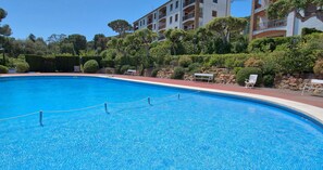 Ein klares, blaues Schwimmbecken, umgeben von einem roten Deck, mit einem Gebäude im Hintergrund.