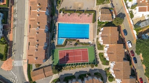 An aerial view of a residential area with a swimming pool, tennis court, and multiple houses with tiled roofs. - Apartment with pool, AC and tennis · Calella (Calella de Palafrugell)