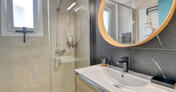 A modern bathroom with a glass-enclosed shower, a vanity with a sink, and a large mirror with a wooden frame. - Apartment with pool, AC and tennis · Calella (Calella de Palafrugell)