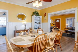 A dining room with a round table, wooden chairs, a ceiling fan, and a mirror on the wall. - Classic Beach House with Game Room & Firepit Near Seaside Beach in Seaside, Oregon (Seaside)