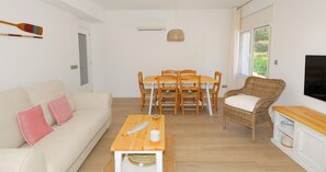 A living room with a sofa, dining table, chairs, a wicker armchair, a TV, and a window. - Renovated apartment with air conditioning, close to restaurants (Calella de Palafrugell)