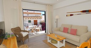 A living room with a sofa, a table, wicker chairs, a balcony with a view of buildings, and a lamp. - Renovated apartment with air conditioning, close to restaurants (Calella de Palafrugell)