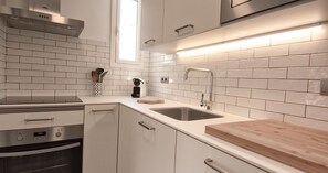 A modern kitchen with white subway tiles, stainless steel appliances, and a wooden countertop. - Renovated apartment with air conditioning, close to restaurants (Calella de Palafrugell)
