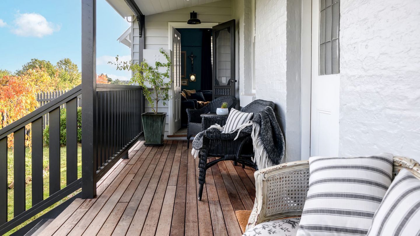 Eine Holzterrasse mit Gartenmöbeln, eine Tür, die zu einem Innenraum führt, und Blick auf Bäume.