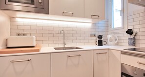 Eine moderne Küche mit weißen Schränken, einer eingebauten Mikrowelle, einem Toaster, einem Wasserkocher und einer Kaffeemaschine.
