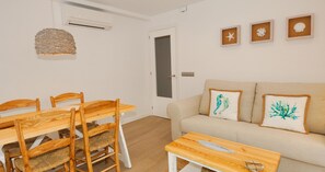 Ein Zimmer mit Esstisch und Stühlen aus Holz, einem beigefarbenen Sofa mit Zierkissen sowie Wandbildern.