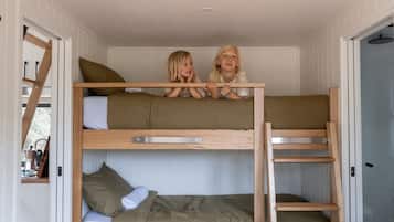 A bunk bed room with two children sitting on top, wooden railings, and white walls.