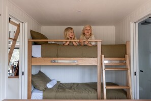 Camera con letto a castello dove due bambini siedono sopra, dotata di ringhiere in legno e pareti bianche.