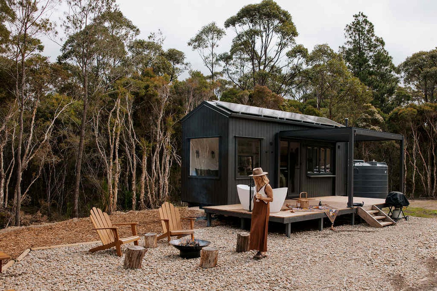 A modern, dark-colored cabin with a deck, surrounded by trees.