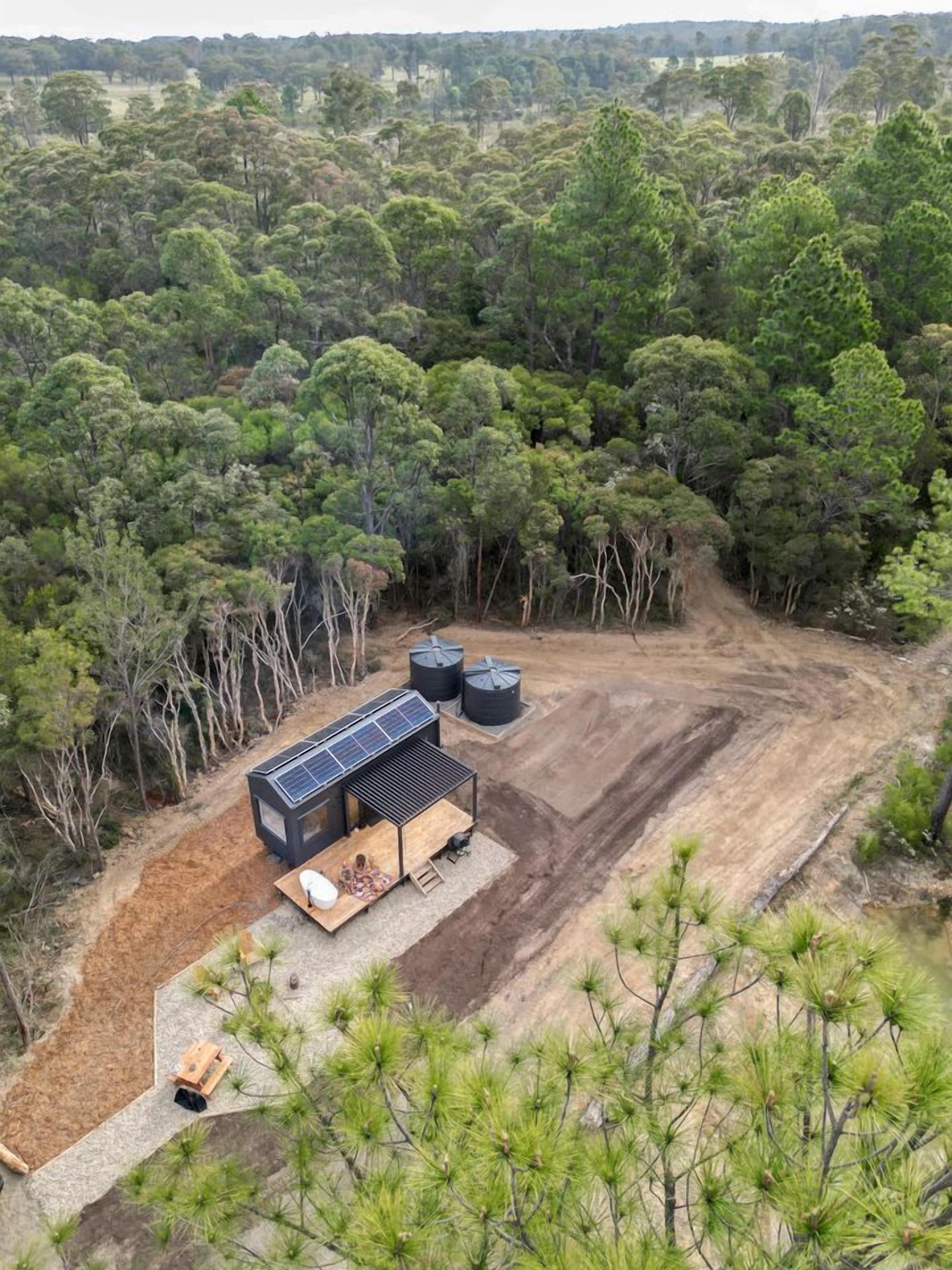 A remote cabin with a solar panel roof, surrounded by dense forest.