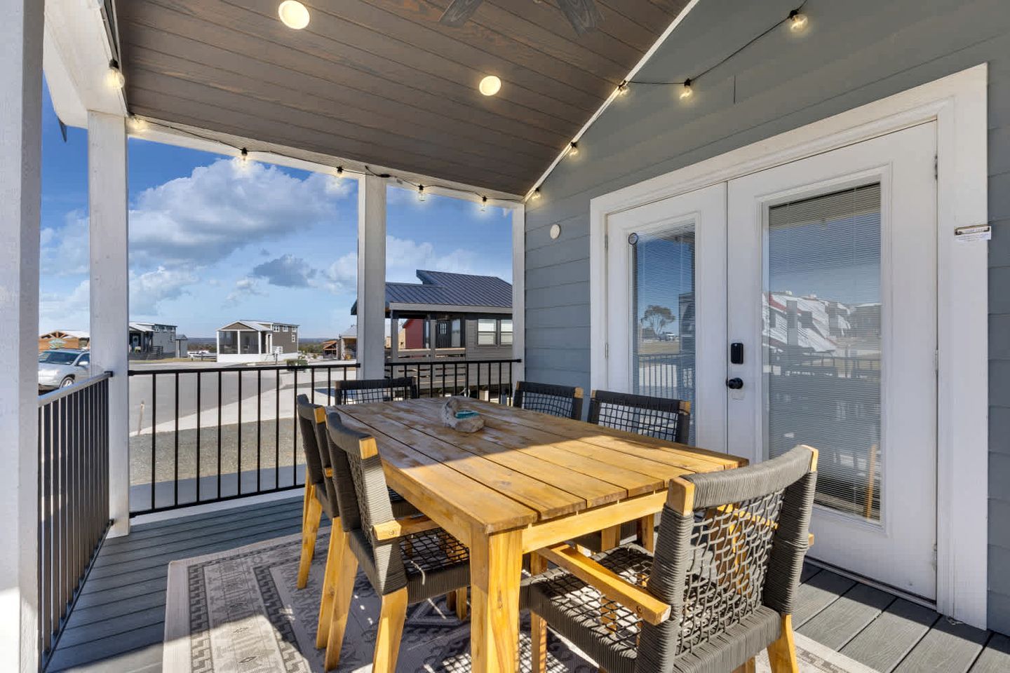 A covered patio with a wooden table and chairs, a view of the surrounding area, and a door with a window.
