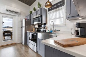 A modern kitchen with stainless steel appliances, a central island, and a view of the beach through the sliding door. - Scenic Tiny Home Retreat with Resort Amenities Near Fredericksburg, TX (Fredericksburg)