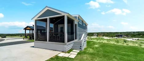 A small, single-story house with a porch, a covered outdoor seating area, and a grassy yard.