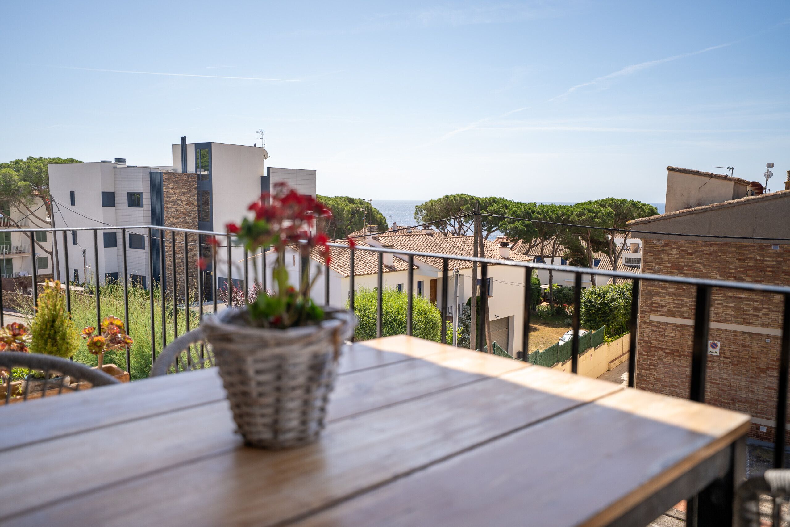 Un balcon avec une table et un pot de fleurs, donnant sur un quartier résidentiel avec des maisons et un ciel dégagé.