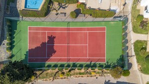 En vy över en tennisbana från ovan, med omgivande grönska och en pool.