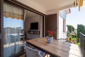 An outdoor dining area with a wooden table and chairs, a wicker basket with flowers, and a view of a garden and buildings in the background. - Renovated flat with sea views and a swimming pool · 150 metres from the beach · Calella (Calella de Palafrugell)