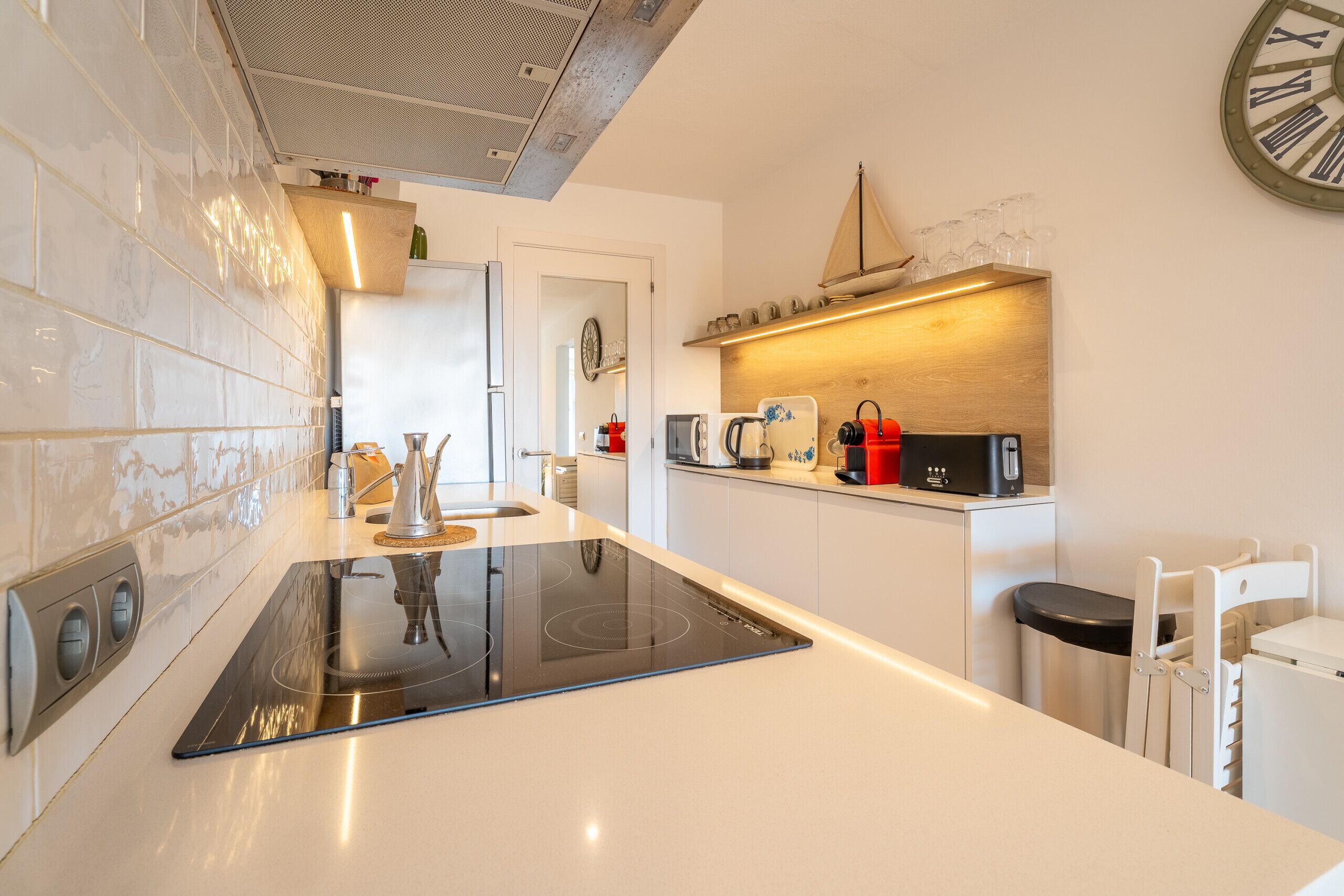 A modern kitchen with a central island, built-in appliances, and a clock on the wall.