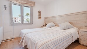 A bedroom with a bed, bedside tables, a nightstand, a window with curtains, and a wall-mounted picture.