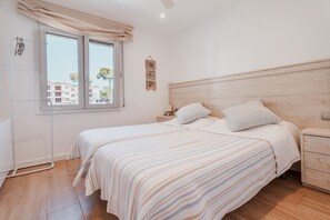 A bedroom with a bed, bedside tables, a nightstand, a window with curtains, and a wall-mounted picture.