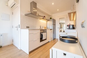 A modern kitchen with white cabinetry, a stainless steel range hood, a built-in oven, a dishwasher, and a black baking tray on the countertop. - Renovated flat with sea views and a swimming pool · 150 metres from the beach · Calella (Calella de Palafrugell)