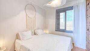 A bedroom with a bed, a wall hanging, a window with blinds, and a bedside lamp. - Apartment with Beautiful Sea Views and Pool in Calella · Perfect to Relax (Calella de Palafrugell)