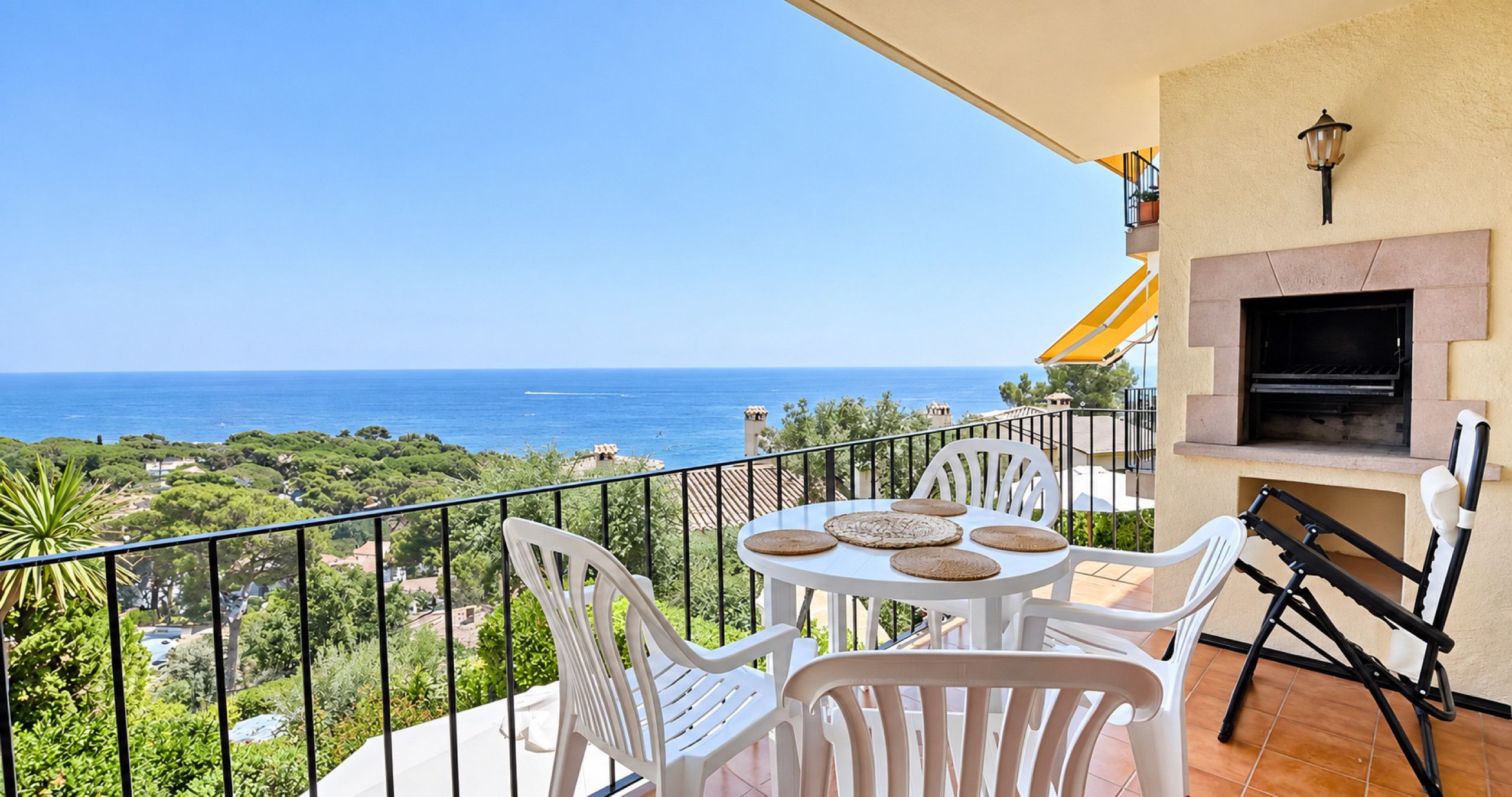 A balcony with a table and chairs, a barbecue grill, and a view of the sea.