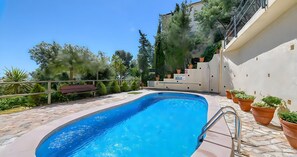 Ein Pool mit einer Metallleiter, umgeben von Topfpflanzen und einer Sitzbank.