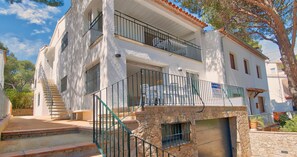 A two-story building with a stone facade, a balcony with a metal railing, and a staircase leading to the entrance. - Spacious family apartment 100m from the sea with terrace, parking and air conditioning (Llafranc)