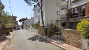 Une rue étroite bordée d’immeubles d’habitation, une entrée fermée par un portail et un ciel dégagé.