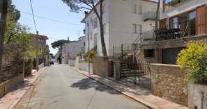 A narrow street with residential buildings, a gated entrance, and a clear sky. - Spacious family apartment 100m from the sea with terrace, parking and air conditioning (Llafranc)