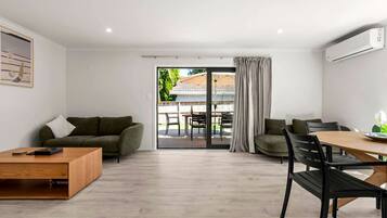 En moderne stue med en sofa, et træ sofabord, et spisebord med stole, og en skydedør af glas der fører ud til en udendørs terrasse.