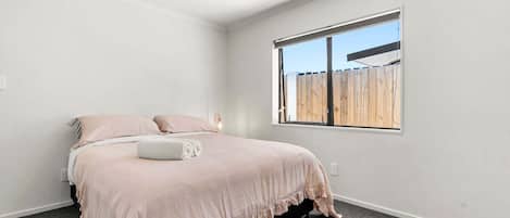 A bedroom with a bed, a window, and a view of a wooden fence.