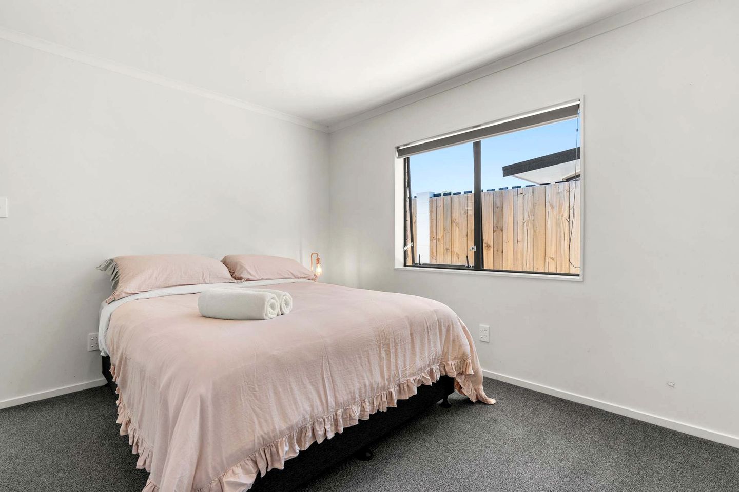 Ein Schlafzimmer mit Bett, Fenster und Blick auf einen Holenzaun.