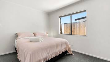 Ein Schlafzimmer mit Bett, Fenster und Blick auf einen Holenzaun.