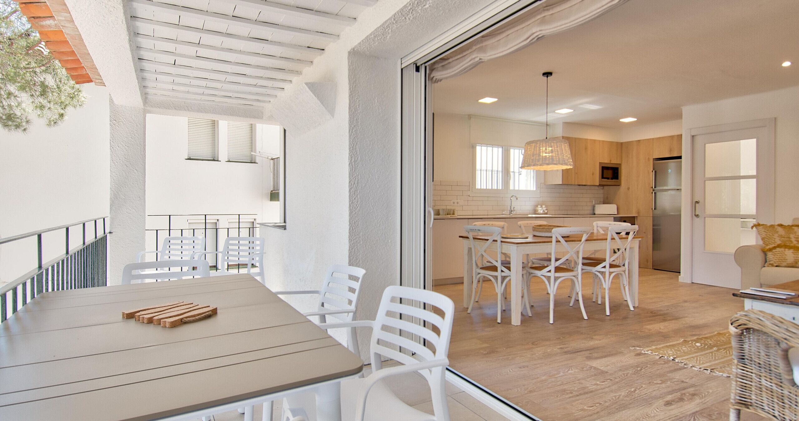 Una cocina moderna con armarios blancos, un comedor con sillas blancas y una mesa de madera.