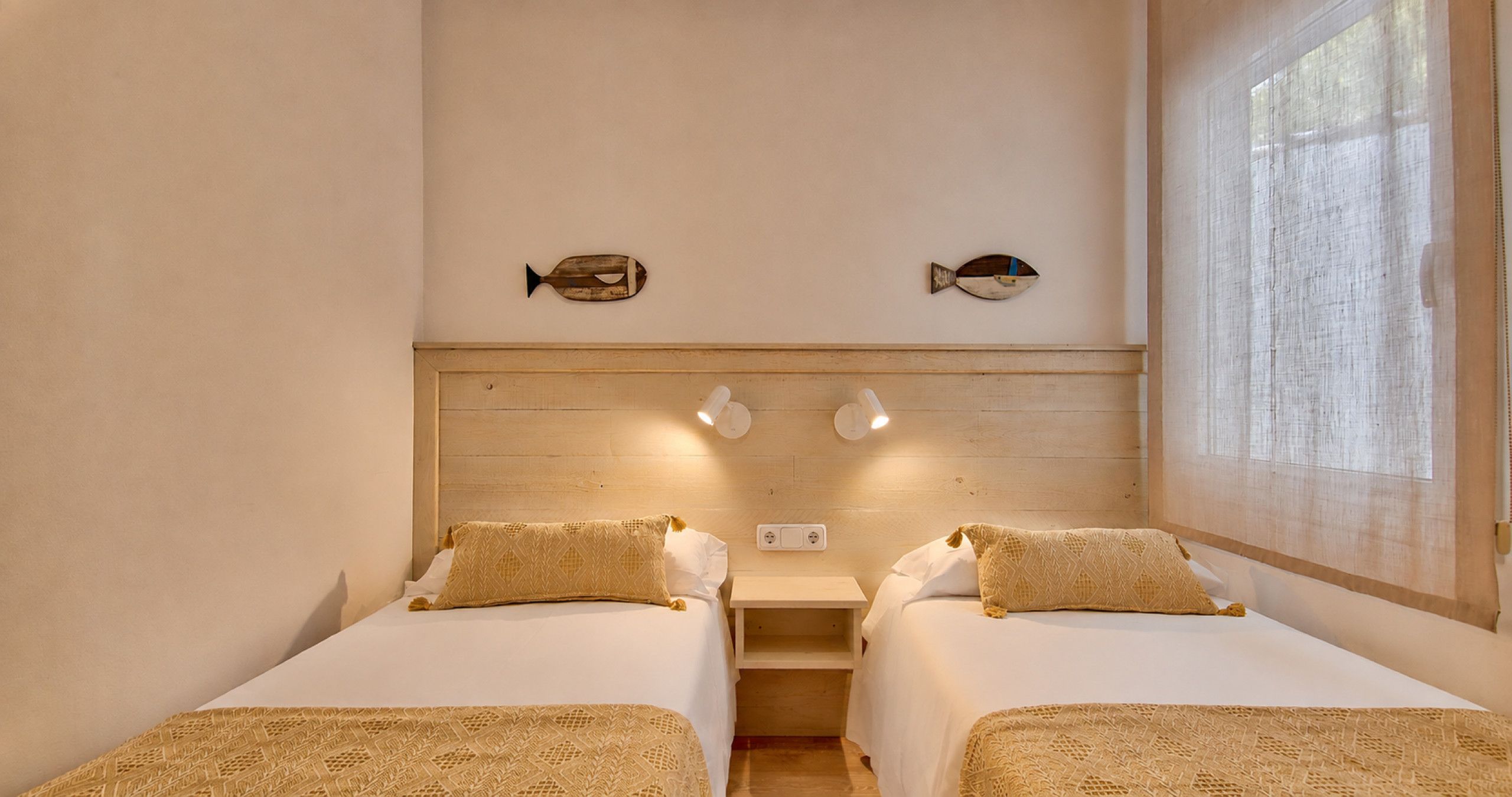 Una habitación con dos camas, un cabecero de madera, luminarias fijadas a la pared y dos adornos en forma de pez.