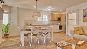 A modern kitchen with white cabinets, a dining table with chairs, a wooden floor, and a hanging light fixture. - Elegant apartment 100m from the beach with parking and air conditioning (Llafranc)
