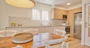 Eine moderne Küche mit einem Holztisch, weißen Stühlen, einem Korbwannen und einem Edelstahlkühlschrank.
