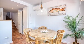 Ein Essbereich mit einem runden Tisch und Korbstühlen, einer Hängelampe und einem Fischgemälde an der Wand.