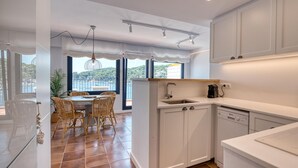 A modern kitchen with white cabinets, a dining area with wicker chairs, and a view of the sea. - Getaway for 2 · Seafront · Calella (Calella de Palafrugell)