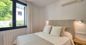 Ein Schlafzimmer mit Bett, einem Fenster mit Vorhängen, einer Klimaanlage und einer Wandleuchte.
