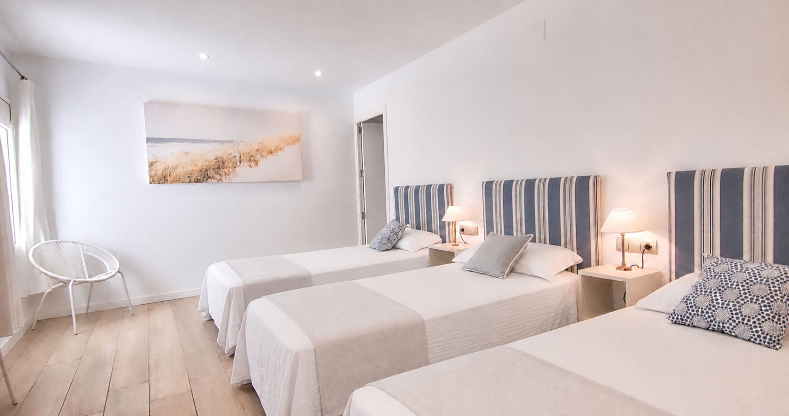 A hotel room with two beds, a chair, and a painting on the wall.