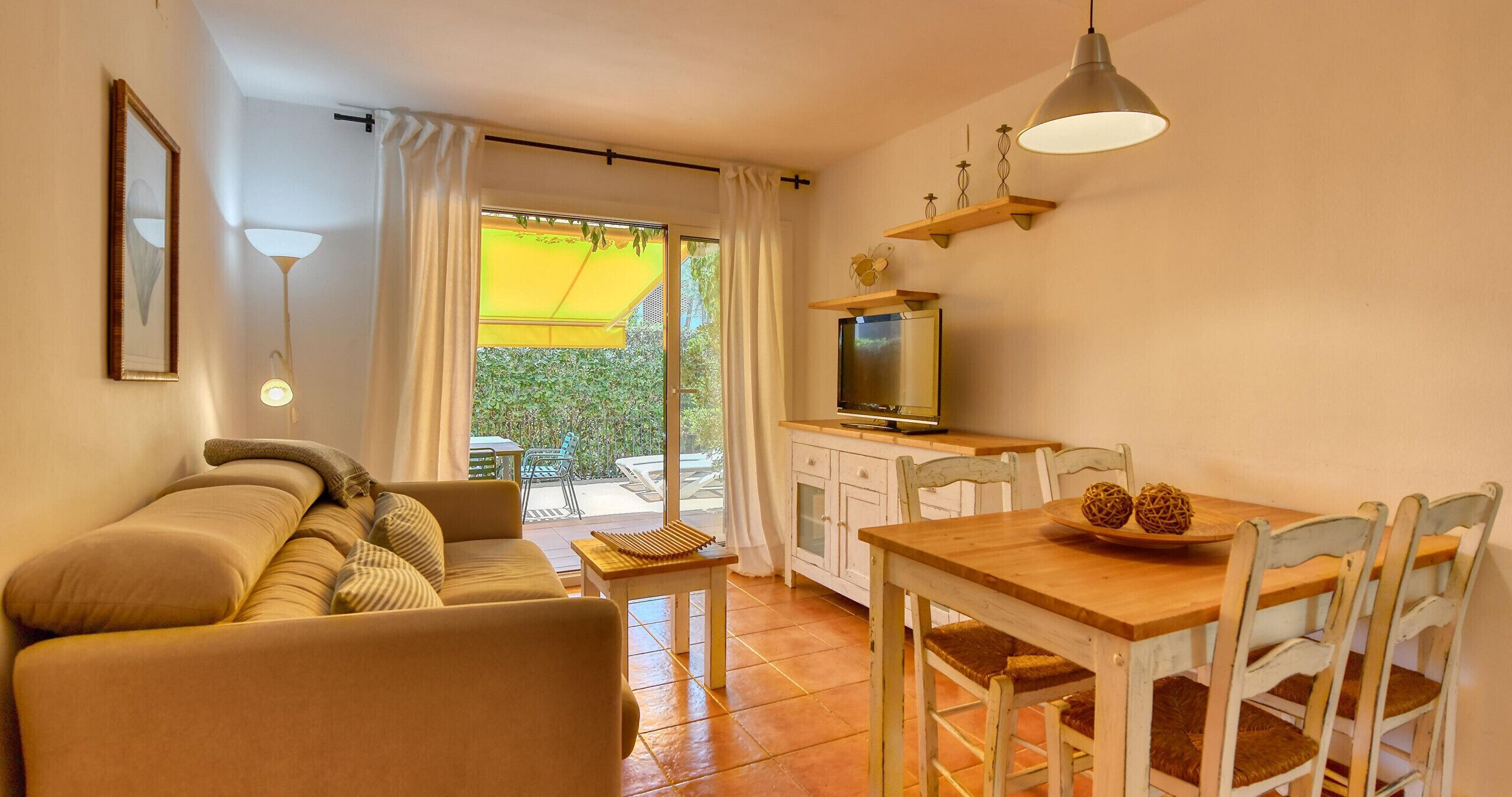 Un salon confortable avec un canapé, une table à manger et des chaises, un téléviseur et un balcon agrémenté d’un parasol jaune.