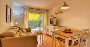 Ein gemütliches Wohnzimmer mit einer Couch, einem Esstisch mit Stühlen, einem Fernseher und einem Balkon mit einem gelben Sonnenschirm.