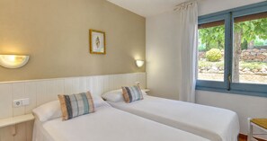 A hotel room with two beds, a window with curtains, a wall-mounted light, and a framed picture. - Cozy apartment with private patio · 150m from the beach · Calella (Calella de Palafrugell)