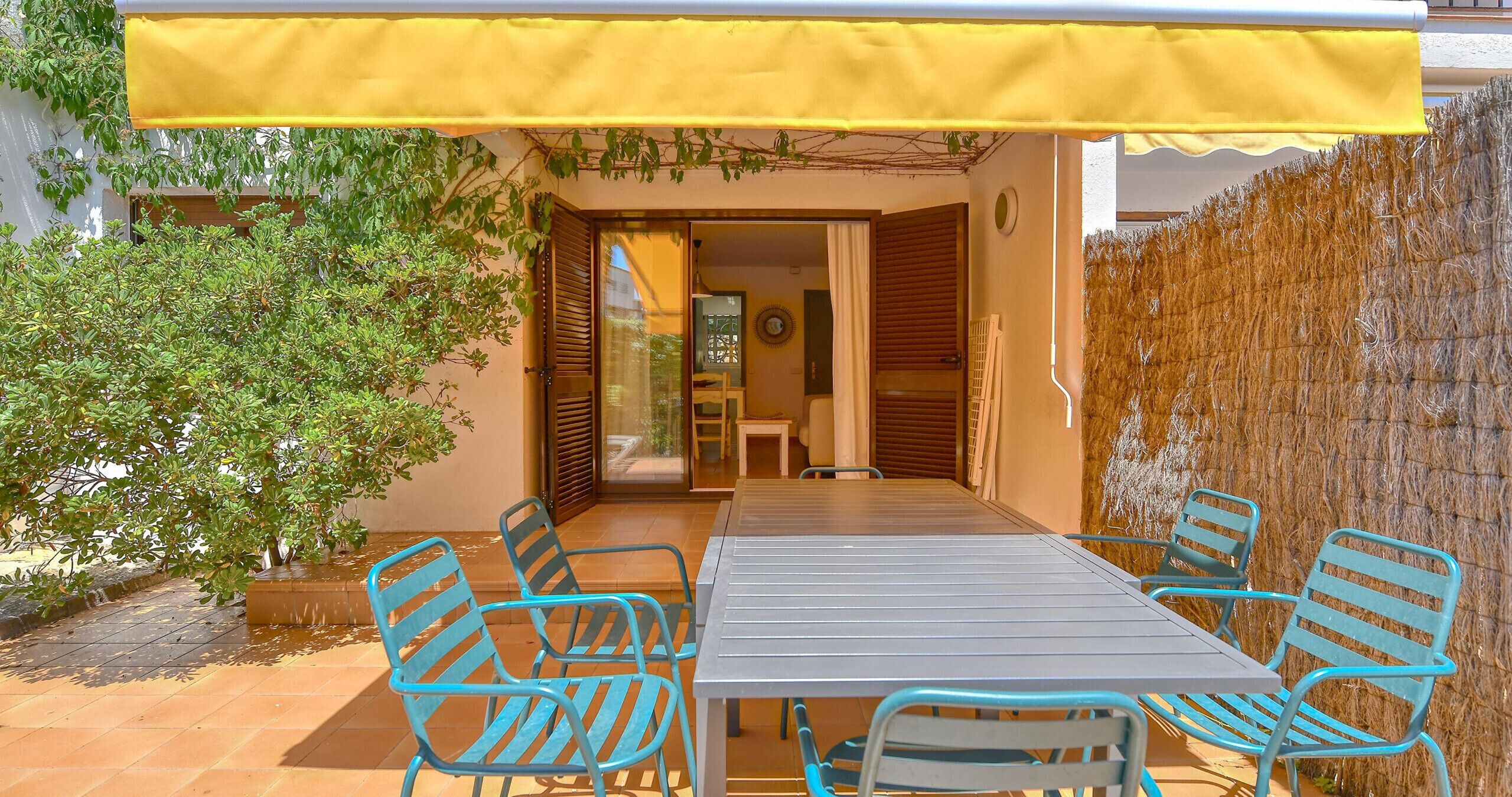 A patio with a table and chairs, a yellow awning, and a view into the house.