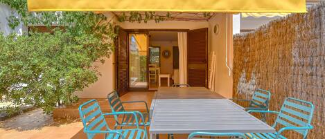 A patio with a table and chairs, a yellow awning, and a view into the house.