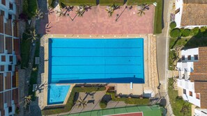 Ein großer rechteckiger Pool mit einer umlaufenden Pflasterfläche, neben einem kleineren Pool und einem Tennisplatz.