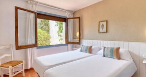 Ein Doppelbett mit zwei Kissen, ein Holzstuhl, ein Fenster mit Vorhängen und ein Wandbild.